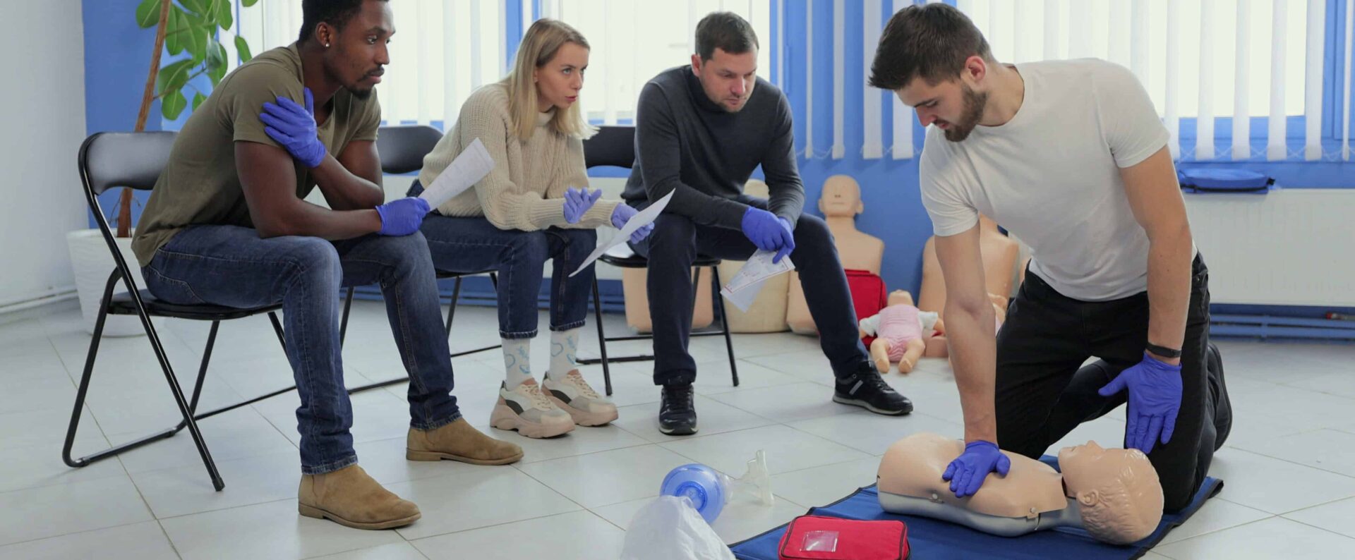 Man instructor showing how to make chest compressions with dummy during the first aid group training indoors.