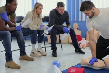 Man instructor showing how to make chest compressions with dummy during the first aid group training indoors.
